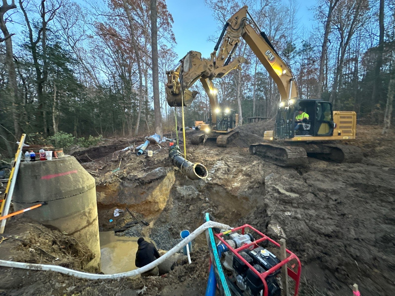An excavator and crew setting a large concrete panel at dusk