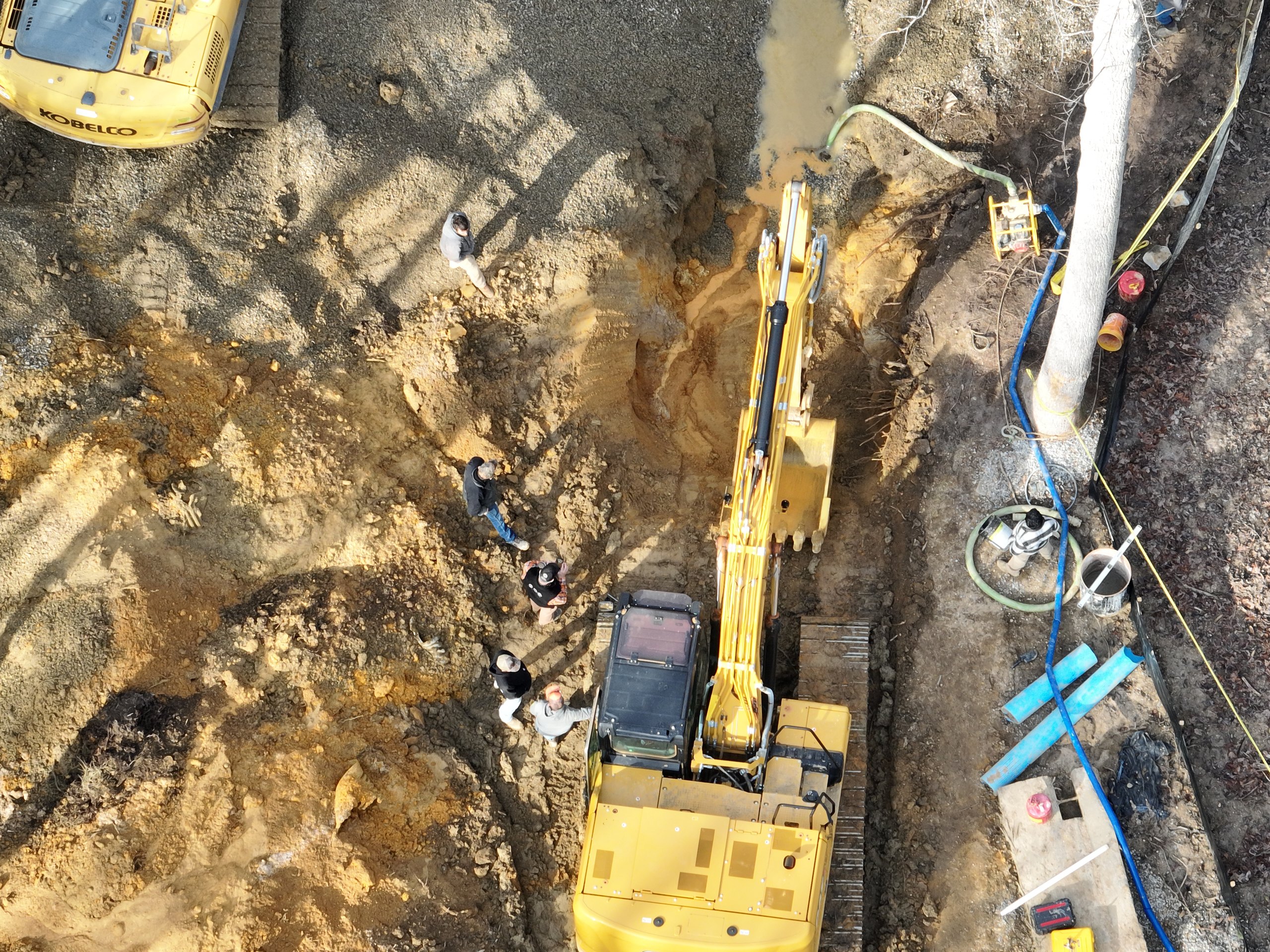 An excavator managing muddy water discharge on a wet site