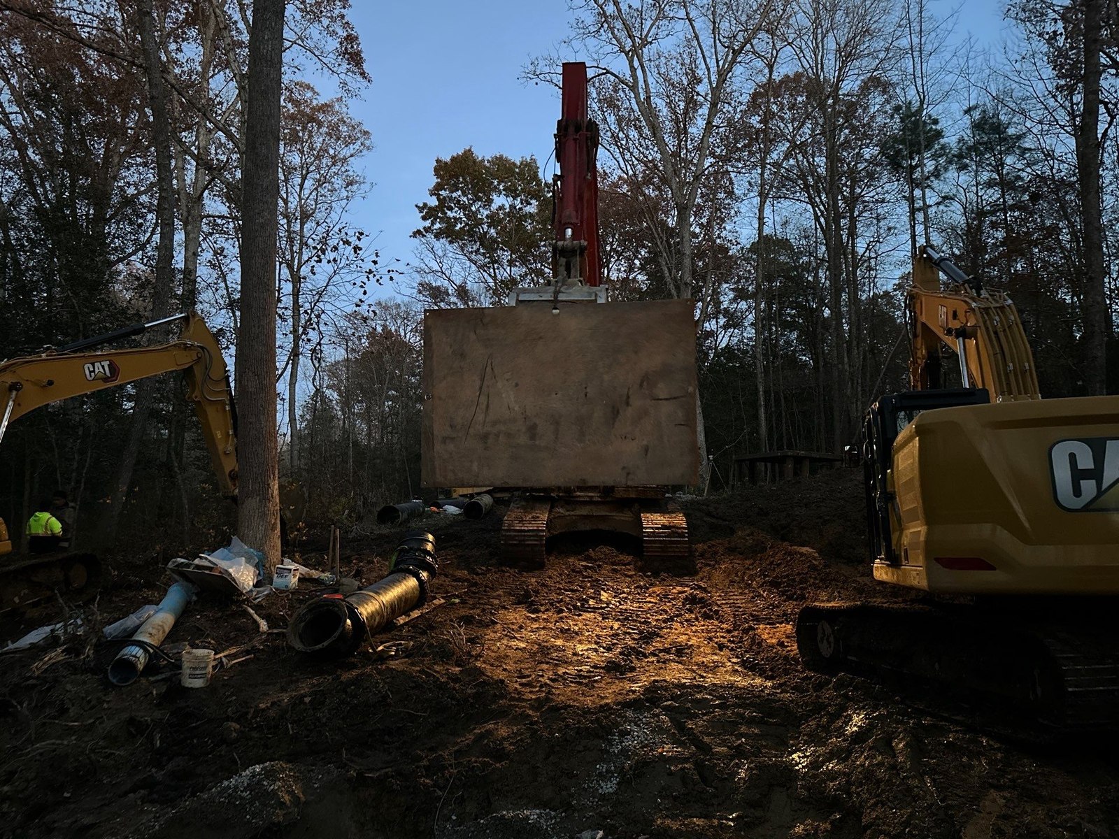 An excavator working a trench after dark under floodlight