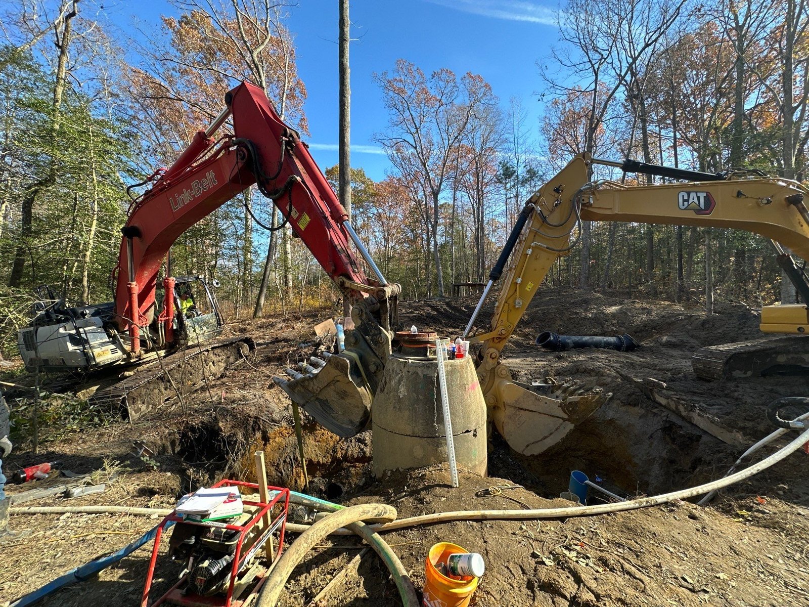 Two excavators flanking a concrete riser structure as a crew works the connection